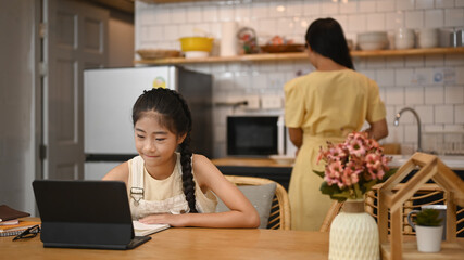 Focused little asian girl watching video lesson on computer laptop, interested in online web virtual class studying from at home.