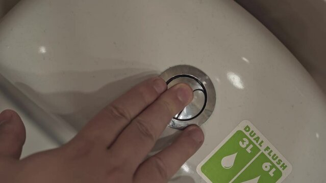 Top view of man's finger presses the toilet flush button. Hygiene in the toilet. Ceramic plumbing. Master checks the serviceability of home equipment after repair or installation.