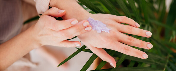 Fototapeta premium Female hands applying purple cream scrub on skin at home. Beauty routine. Skincare concept