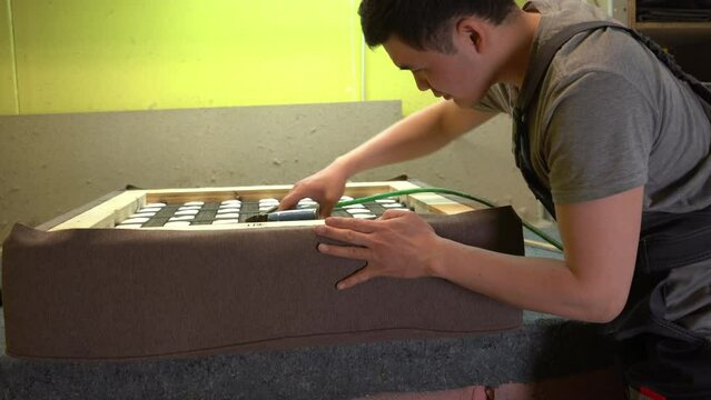 Furniture upholstery. A carpenter fixes the fabric with a pneumatic stapler.