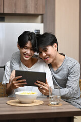 Happy LGBT couple enjoying the movie on digital tablet while spending leisure time together at home