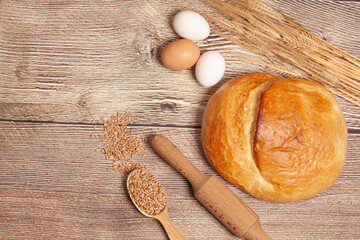 Loaf of round bread with egg, wheat ears, grains, rolling pin on a wooden table top view. Culinary background, baking concept