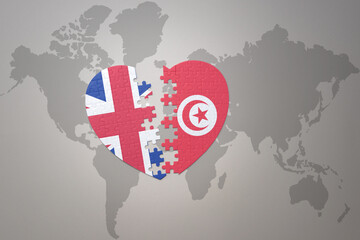 puzzle heart with the national flag of tunisia and great britain on a world map background. Concept.