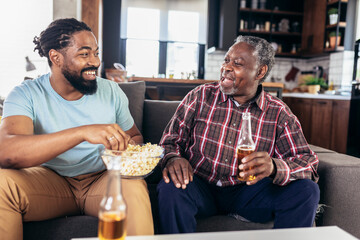 Excited old father and son watching tv, eating popcorn snack, having fun at home