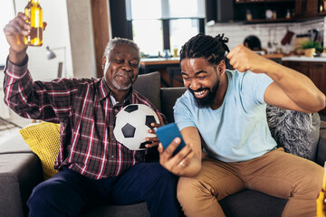 Man with senior father scream support favorite sports team together use smartphone app to online bet