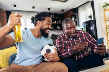 Man with senior father scream support favorite sports team together use smartphone app to online bet