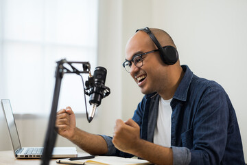 Content creator asia man host streaming his a podcast on laptop with headphones and condenser microphone interview guest conversation at home broadcast studio. Male blogger recording voice over radio