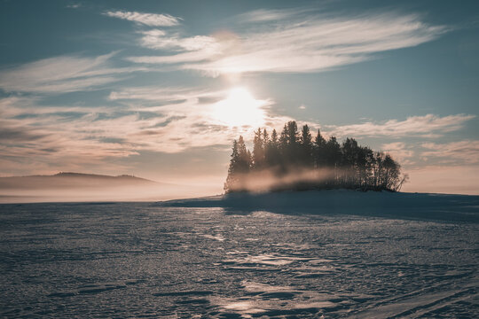 Fog on lake Storsjö during a beautiful sunrise close to Ljungdalen during snowy winter. Frozen lake and spruce trees.