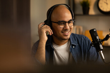 Young asian man host streaming podcast with condenser microphone work on laptop at small broadcast...