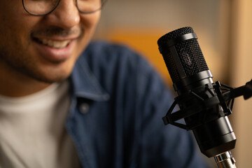 Young asian man host streaming podcast with condenser microphone work on laptop at small broadcast...