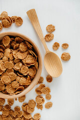 Crispy healthy dry cereal flakes in a wooden bowl with wooden spoon on white background