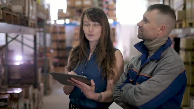 Workers inside warehouse check delivered cargo with waybill. female manager in a large warehouse distribution retail center explains to employee arrangement of cardboard boxes on shelves