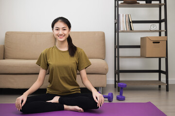 Young asian sport woman sitting on the yoga mat practicing meditation. Fitness or exercise at home. Beautiful female relaxing after workout.