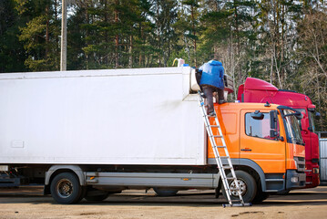 Worker with ladder on truck head improve truck refrigeration systems. Man with equipment repair...