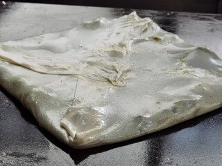 The preparation of a Turkish Katmer dessert, the content of which is dough, cheese and pistachios.