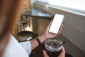 Mockup image of a woman holding mobile phone with blank desktop screen while drinking coffee