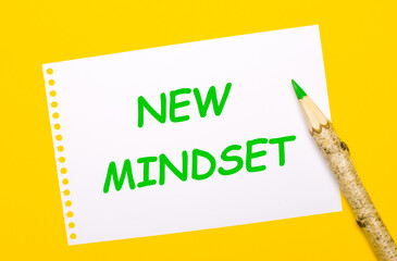 On a bright yellow background, a large wooden pencil and a white sheet of paper with the text NEW MINDSET