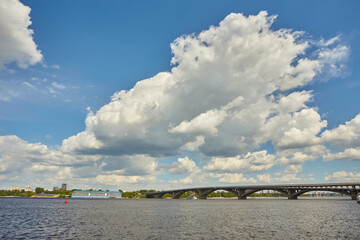 View from the right bank of the Dnieper river over the first metro bridge in Kyiv city with blue subway train, motorboat under it and hotelship behind.
