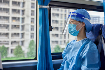 Female medical worker in medical mask and protective shield on her head makes her way to the hospital during the COVID-19 pandemic.