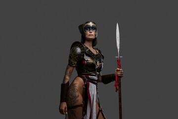 Portrait of ancient amazon with spear dressed in armour against grey background.