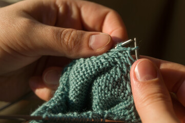 Obraz premium Close-up hand knitting. Hobbies, handicrafts. Knitting warm clothes from woolen fine yarn by hand on metal needles. Selective focus