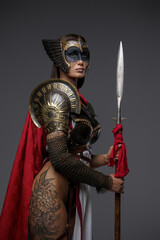 Shot of female warrior with painted face dressed in armor and red cape against grey background.
