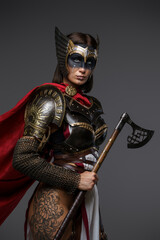 Shot of female viking warrior with axe and tattooed body isolated on grey background.