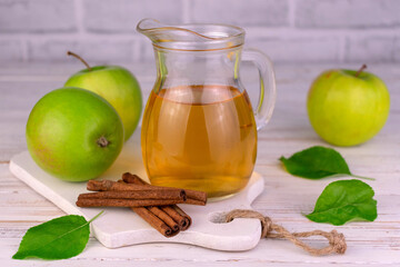 Fresh apple juice in a glass decanter and cinnamon sticks.
