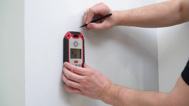 The male hand with electronic wall scanner. Male hand using stud finder to search apartment wall for studs and live wires.
