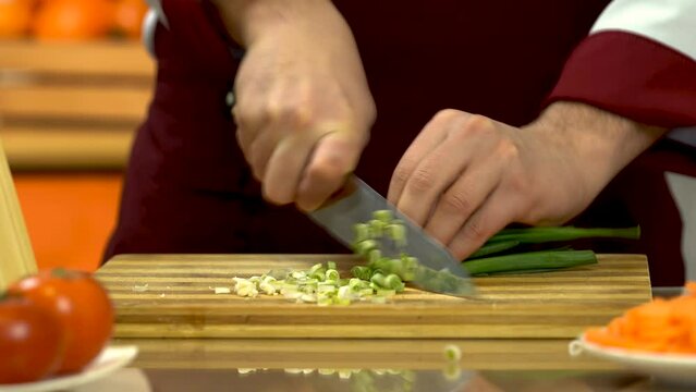 Man's hand cutting fresh green onion. Chef's chopping green onion. Cutting vegetables Healthy Food Concept. A young man prepares food in the kitchen for salad or soup. 