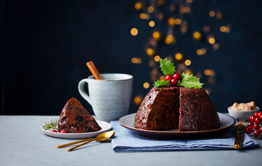 Christmas pudding, fruit cake with cup of tea. Traditional festive dessert. Dark background with lights garland. Copy space.