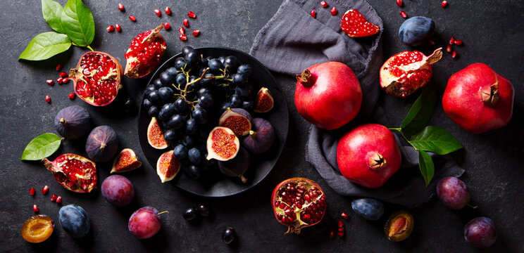 Fruits assortment, pomegranates, grapes, figs, plums on black plate. Dark background. Top view.