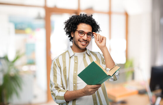 education, business and people concept - happy smiling young man in glasses reading book over office background