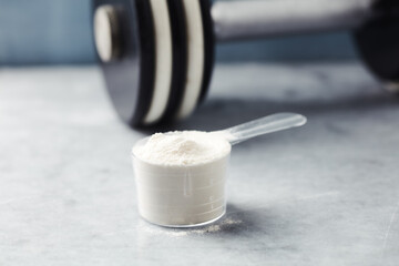 Scoop of Whey Protein and a dumbbell. Bodybuilding food supplements on stone background. Soft...
