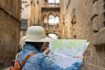 Latin tourist consulting the street map in the Gothic Quarter of Barcelona (Spain), selective focus on the back, travel concept.