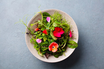 Green salad leaves, sprouts with edible flowers in bowl. Grey background. Close up. Top view. - 506595331