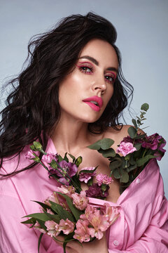 Beautiful brunette girl iwith a gentle pink romantic make-up, pink lips, holding flowers. The beauty of the face.