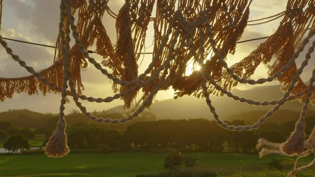 Festive string lights illumination on boho tipi arch decor on outdoor wedding ceremony venue. Vintage string lights bulb garlands shining above chairs at summer rural wedding.