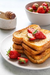 Stack of french toast covered with strawberries and honey on light background. Morning breakfast, brunch or lunch concept. Selective focus.