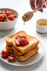 Stack of homemade french toast with fresh strawberries. Process of pouring honey on pieces of toast. Honey drips from wooden spoon in hand. Selective focus.