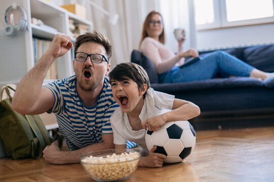 cheerful father and son watching soccer game at home