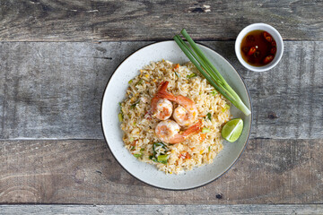 Thai fried rice with shrimp, green onion, lime, chili and fish sauce on a wooden table, top view, copy space.
