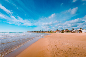Sandy beach by the sea at Donnalucata, Sicily, with blue skies and clouds - obrazy, fototapety, plakaty