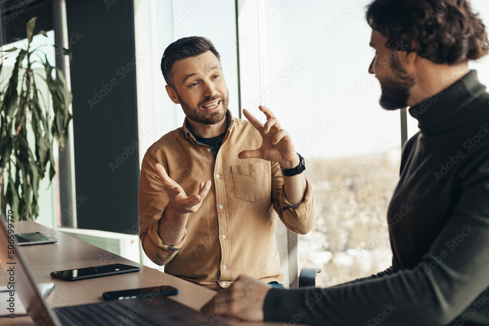 Poster business partners sitting at desk with laptop computer and discussing modern strategies at company o