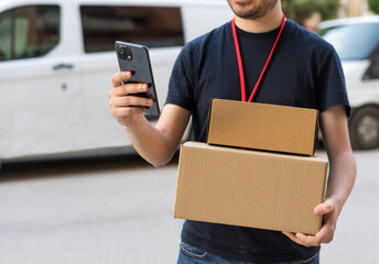Detalle de repartidor, mirando el teléfono móvil, con las cajas de cartón, para ver ubicación de la entrega.