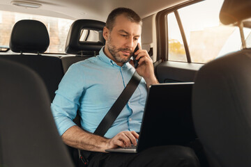 Fototapeta na wymiar Businessman using laptop talking on smartphone while going by car