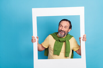 Portrait of cheerful excited person hold paper frame look interested empty space isolated on blue...