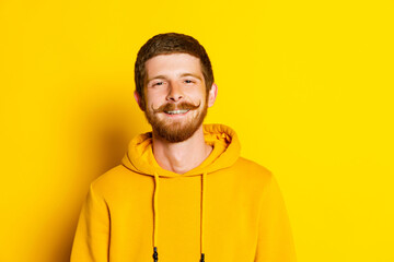 Studio shot of young happy man in yellow hoodie looking at camera isolated on bright background. Concept of human emotions, facial expression, sales, ad, fashion and beauty