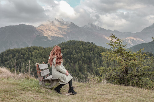 Woman sitting on a bench enoying the view of the nature and mountains.
