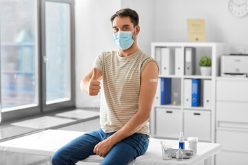 health, medicine and pandemic concept - happy male patient in mask with patch on his arm after...